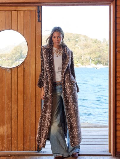 Long animal-print coat worn at a lakeside cabin door